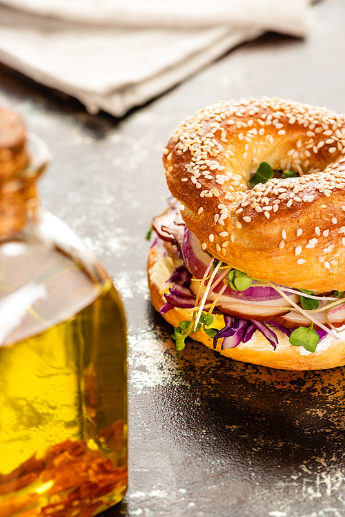 selective focus of oil and fresh delicious bagel with meat, red onion, cream cheese and sprouts on textured surface