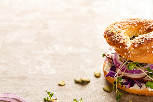 fresh delicious bagel with meat, red onion, cream cheese and sprouts on textured surface
