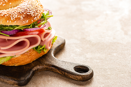 fresh delicious bagel with sausage on wooden cutting board on textured surface