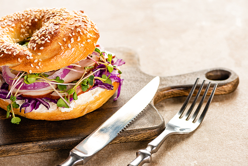 fresh delicious bagel with meat, red onion, cream cheese and sprouts on wooden cutting board with cutlery