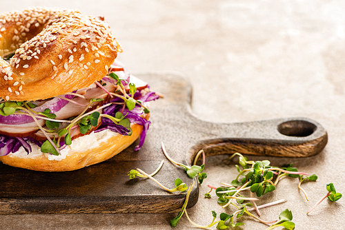 fresh delicious bagel with meat, red onion, cream cheese and sprouts on wooden cutting board