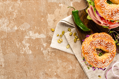 top view of fresh delicious bagels on wooden cutting board on napkin with pumpkin seeds on aged beige surface