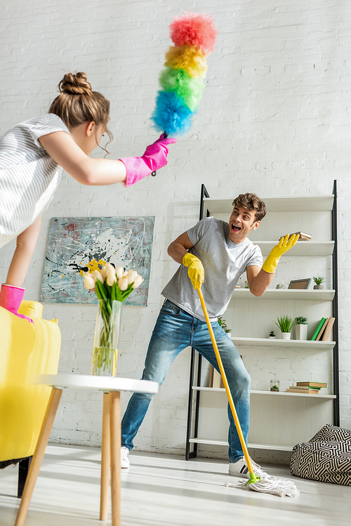 selective focus of handsome man looking at young woman doing spring cleaning in apartment