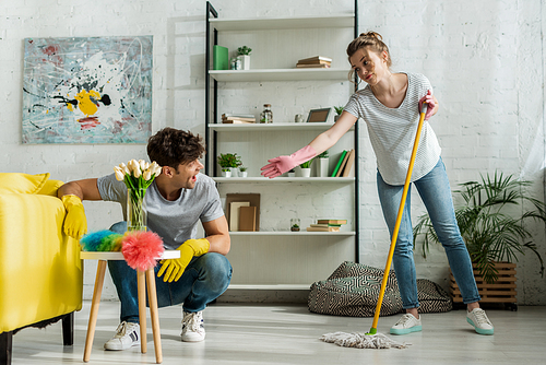 attractive girl with outstretched hand looking at man cleaning at home