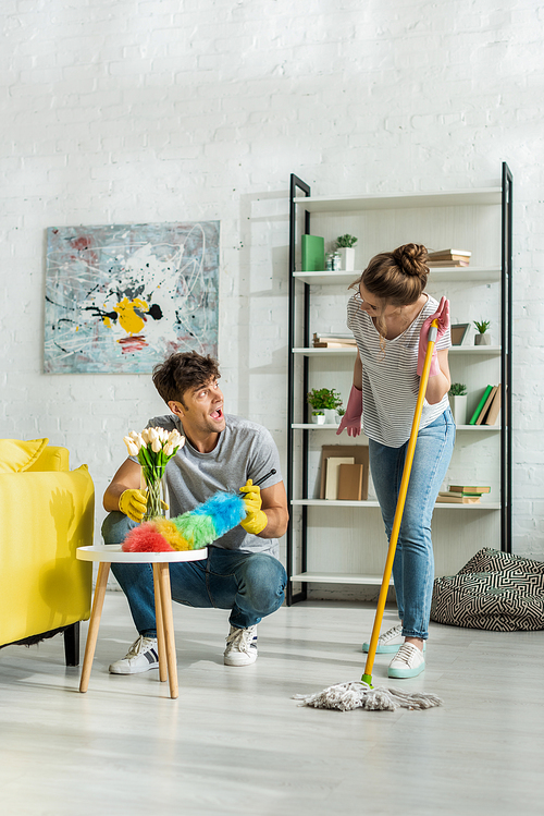 excited man and happy woman looking at each other while cleaning living room