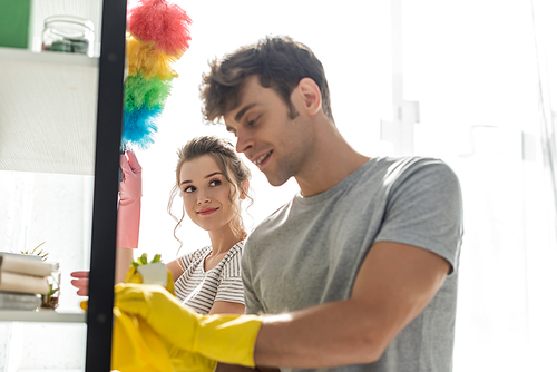 selective focus of attractive girl looking at happy man cleaning rack at home