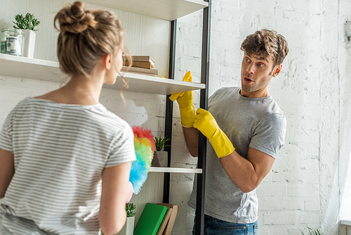 selective focus of surprised man cleaning rack shelves near girl at home
