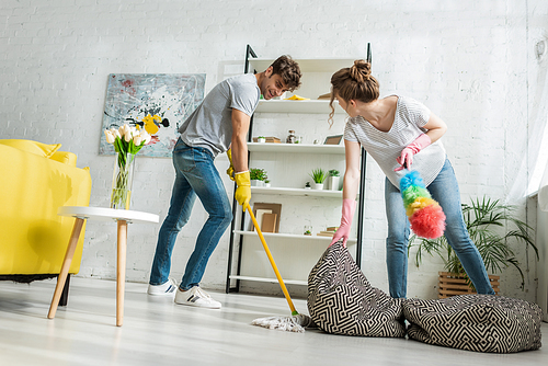 woman holding bean bag chair while man cleaning floor with mop
