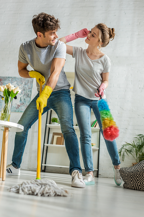 selective focus of cheerful girl and man looking at each other while cleaning in living room