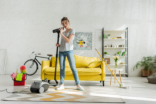 attractive young woman holding vacuum cleaner in living room