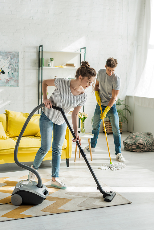 attractive girl using vacuum cleaner near man washing floor with mop