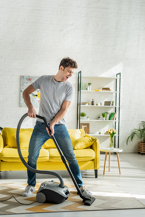 handsome man with opened mouth using vacuum cleaner in living room