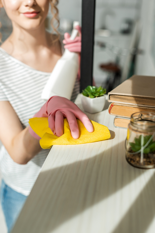 cropped view of woman cleaning shelve with books and plants