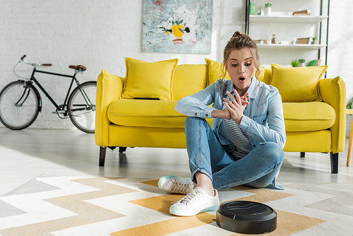 surprised girl looking at robotic vacuum cleaner on carpet in living room