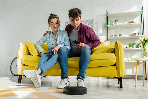 man and young woman looking at robotic vacuum cleaner washing carpet in living room