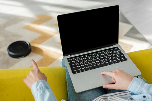 cropped view of woman pointing with finger at robotic vacuum cleaner near laptop with blank screen