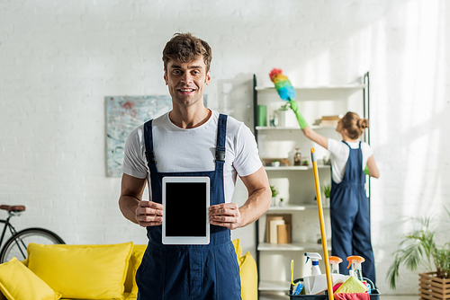 selective focus of happy and handsome cleaner holding digital tablet with blank screen