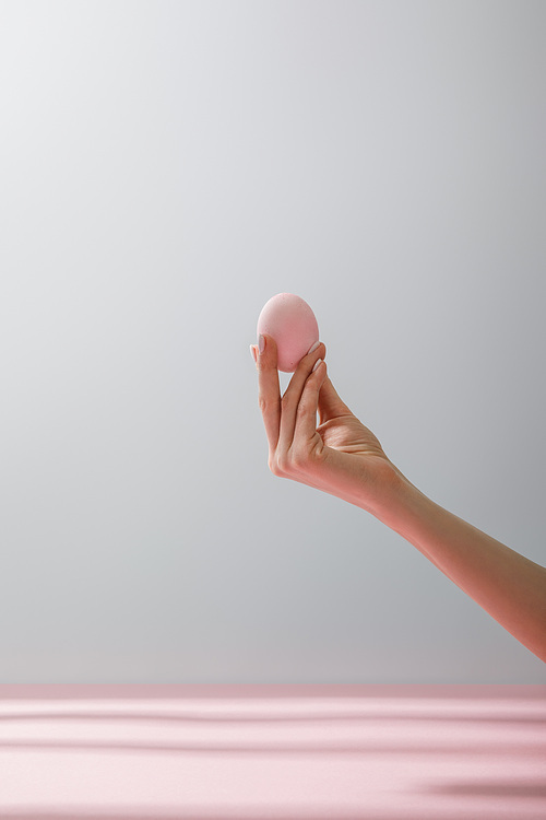 Partial view of woman holding chicken egg isolated on grey background