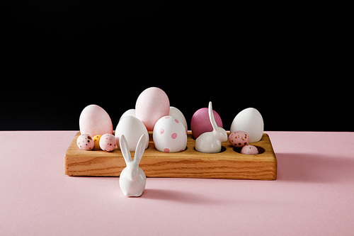 Decorative white bunnies and easter eggs on wooden board on pink and black background