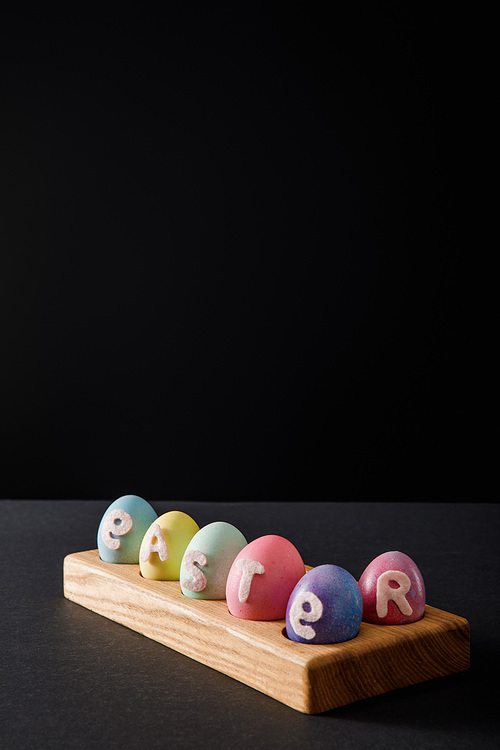 Painted chicken eggs with easter lettering on wooden board on grey and black background