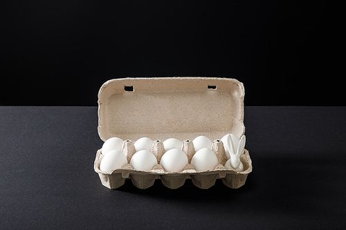 Egg tray with chicken eggs and decorative bunny on grey and black background
