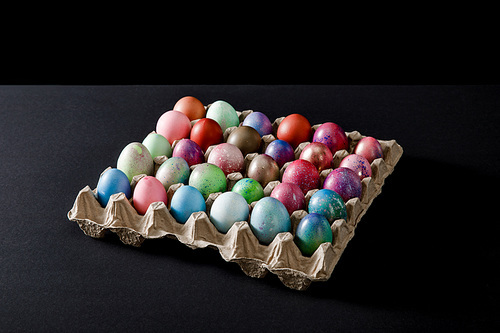 Egg tray with colorful Easter eggs on grey and black background