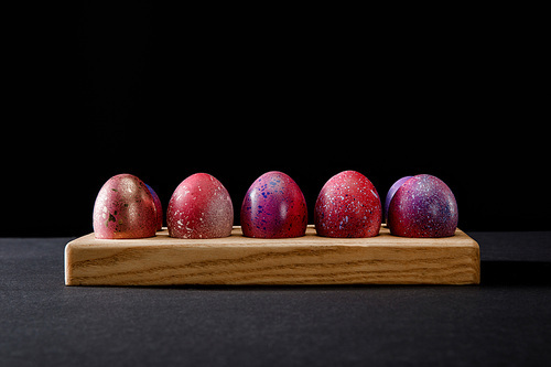 Colorful Easter eggs on wooden board on black background