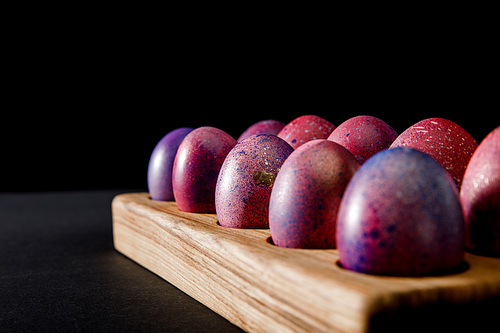 Selective focus of colorful Easter eggs on wooden board on grey and black background