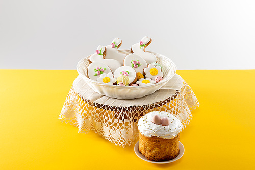 Delicious cookies in wicker basket on round board near easter cake isolated on grey background