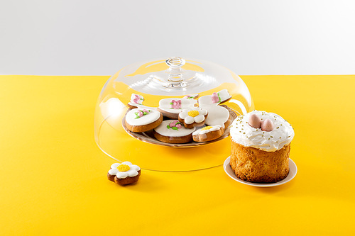 Bowl with tasty cookies covered by glass lid near easter cake isolated on grey background