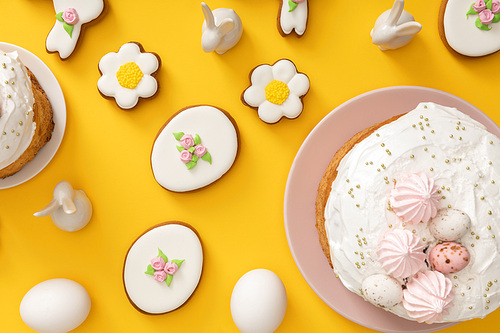 Top view of easter cakes, chicken eggs, cookies and decorative bunnies on yellow background
