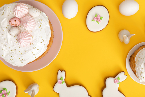 Top view of easter cakes with chicken eggs, cookies and decorative bunnies on yellow background