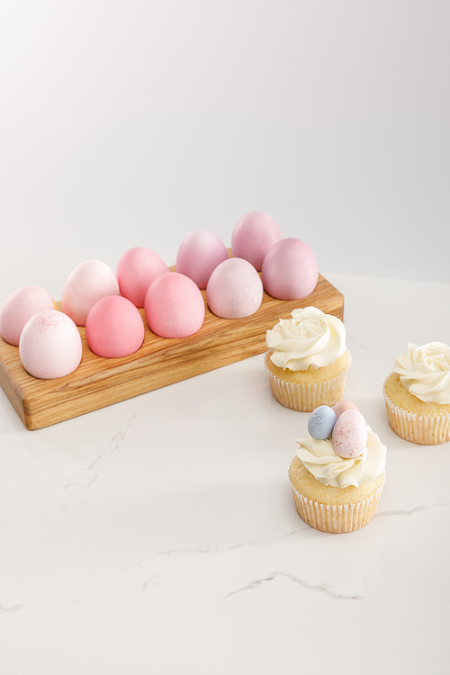 Easter eggs on egg tray with tasty cupcakes on grey background