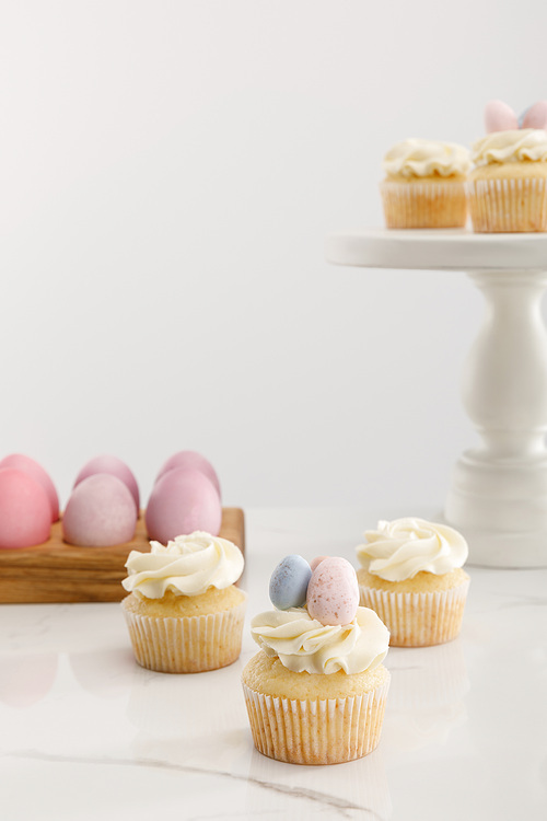 Delicious Easter cupcakes on surface and cake stand near painted chicken eggs on grey background