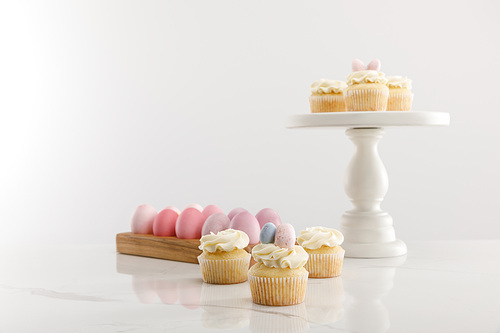 Selective focus of delicious Easter cupcakes on surface and cake stand and painted chicken eggs on grey background