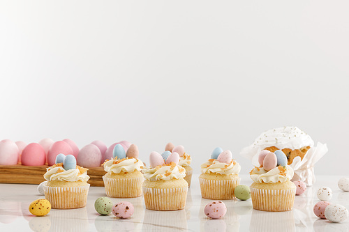 Delicious cupcakes with colorful painted chicken and quail eggs near easter cake isolated on grey