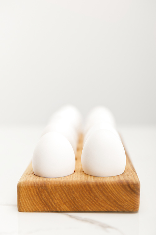 Selective focus of wooden board with chicken eggs on grey background