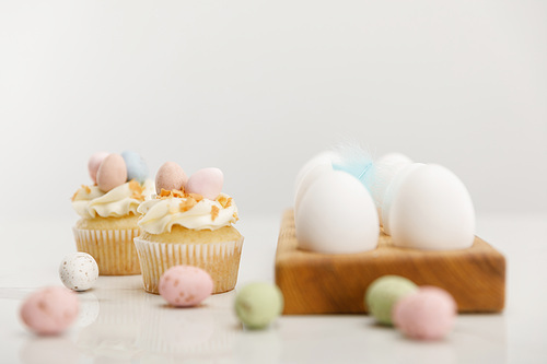 selective focus of colorful quail and chicken eggs on wooden board with . cupcakes on grey background
