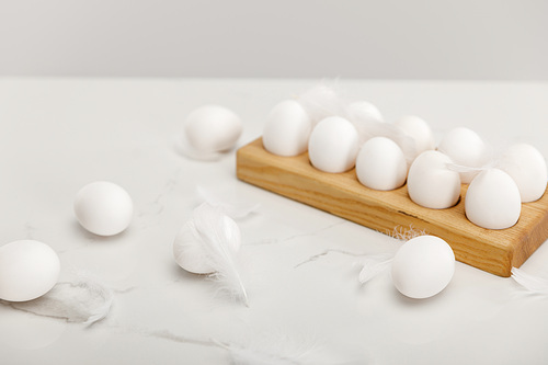Selective focus of chicken eggs on wooden board and feathers isolated on grey