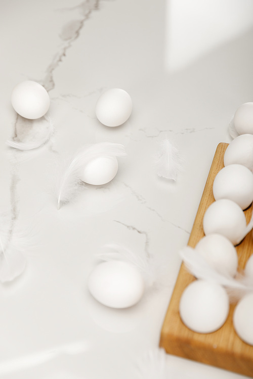 Chicken eggs on wooden egg tray with feathers on white background