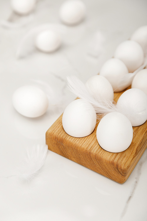 Selective focus of wooden egg tray with eggs and feathers on white background