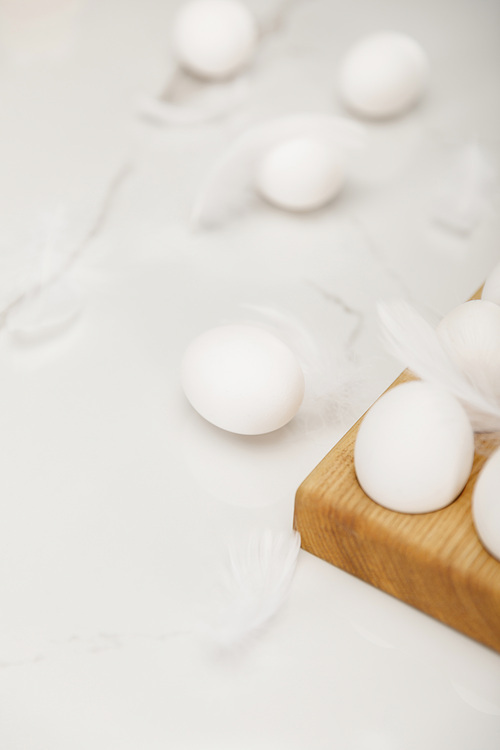 Selective focus of eggs on wooden egg tray and feathers on white background