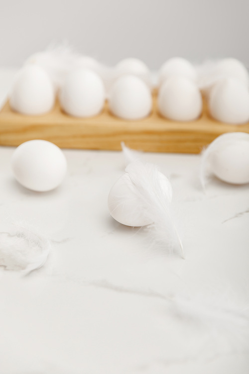 Selective focus of eggs on wooden board with feathers on white background