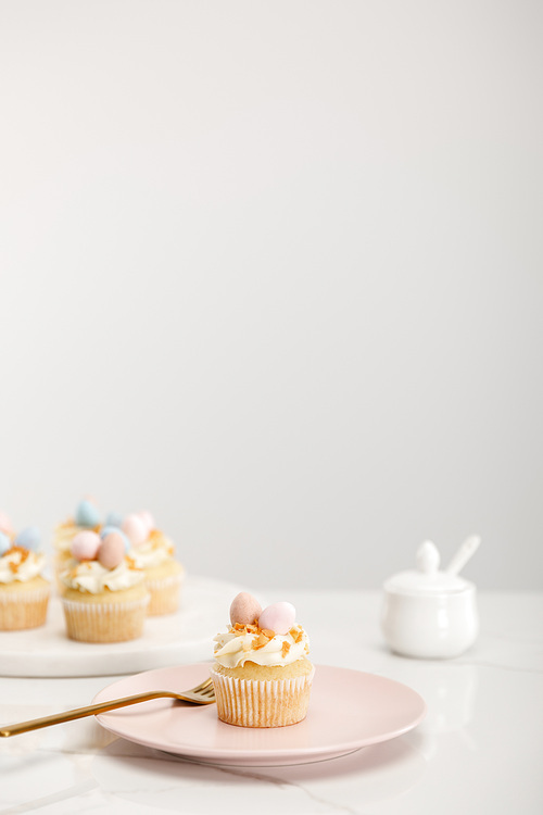 Selective focus of cupcakes on plate and round board near sugar bowl on grey background