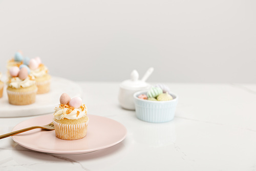 Selective focus of easter cupcakes on plate and round board near sugar bowl on grey background