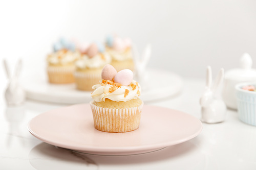 Selective focus of cupcake on plate with decorative bunnies on grey background