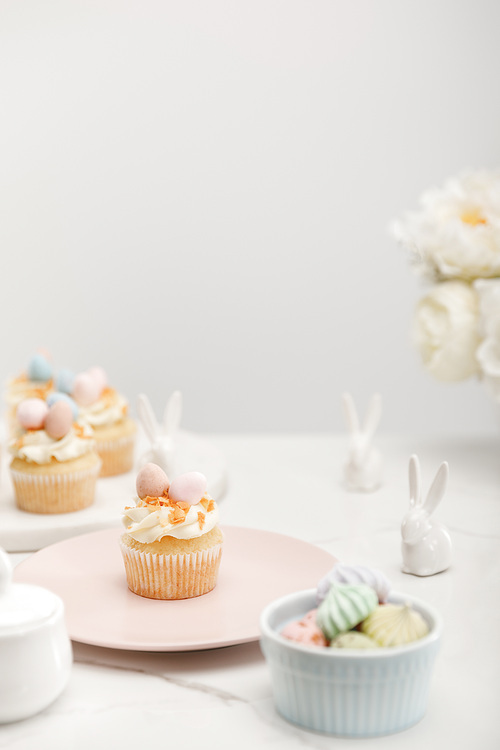 Selective focus of cupcakes with decorative bunnies, bowl with meringues and flowers on grey background