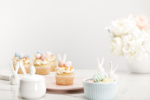 Selective focus of cupcakes, decorative bunnies, sugar bowl, meringues and vase with flowers on grey background