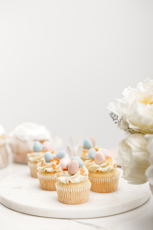 Selective focus of cupcakes on round board with flowers on grey background
