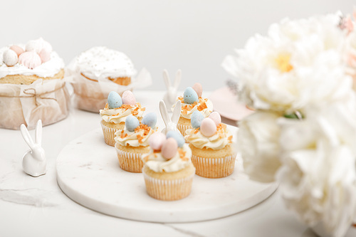 selective focus of cupcakes with decorative bunnies on round board, flowers and . cakes isolated on grey